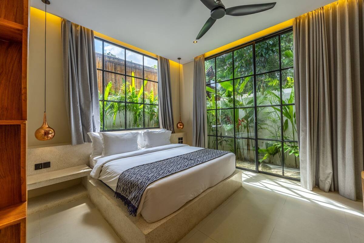 A bedroom with a bed, a ceiling fan, and large windows with curtains.