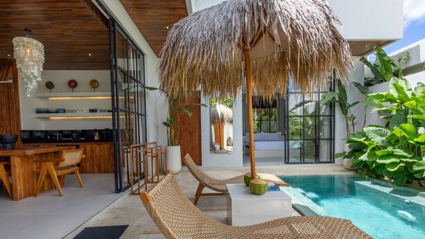 A modern outdoor pool area with lounge chairs, a bar, and a large umbrella. - Aricivillas (Pecatu)