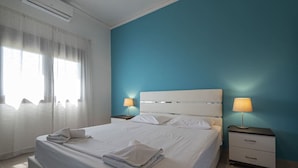 Een hotelkamer met een groot bed, twee nachtkastjes, een raam met dunne gordijnen en een blauwe accentmuur.