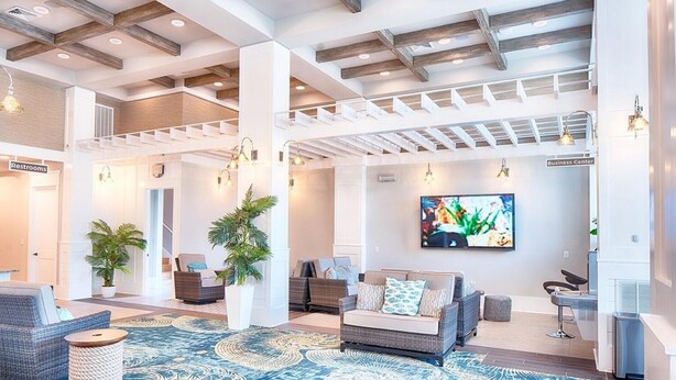 A spacious lobby with a high ceiling, wooden beams, a large TV screen, and a seating area with wicker furniture.