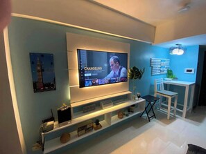 A modern living room with a flat-screen TV mounted on the wall, a small table with a chair, and a decorative plant. - One Palm Tree Villas Condotel Near NAIA3 (Pasay)