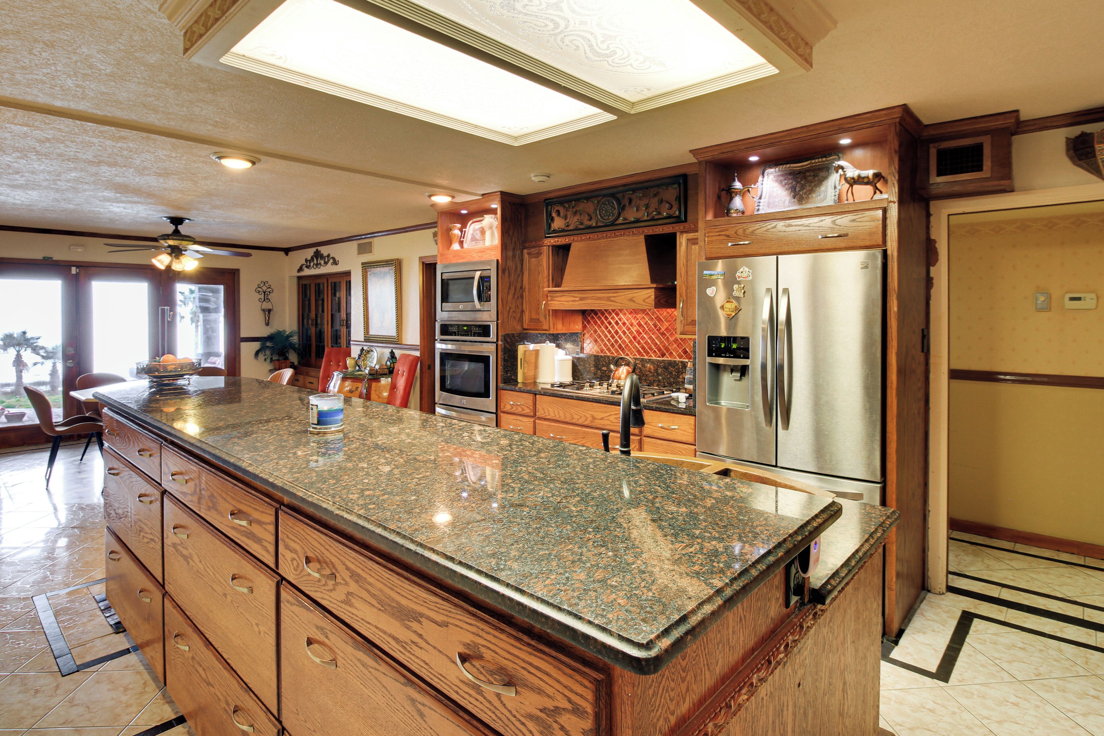 A kitchen with granite countertops, stainless steel appliances, wooden cabinetry, and a ceiling fan.