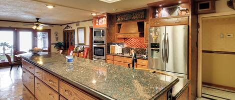 A kitchen with granite countertops, stainless steel appliances, wooden cabinetry, and a ceiling fan.