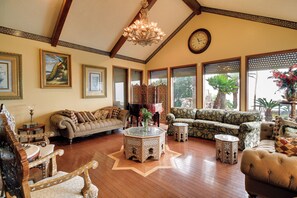 Ein geräumiges Wohnzimmer mit hohen Decken, Holzboden und verschiedenen Sitzmöglichkeiten, darunter eine Couch, Sessel und eine Zweiseiter-Couch.