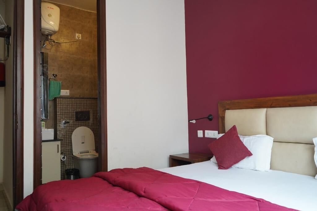 A hotel room with a bed, a nightstand, a lamp, and a bathroom visible through an open door.