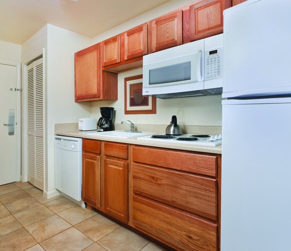 A kitchen with wooden cabinets, a microwave, a coffee maker, a kettle, and a dishwasher.