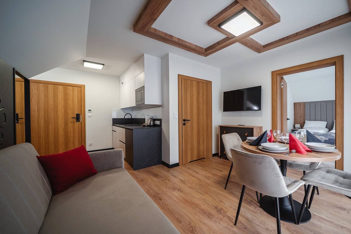 A modern hotel room with a kitchenette, dining area, and a large mirror.