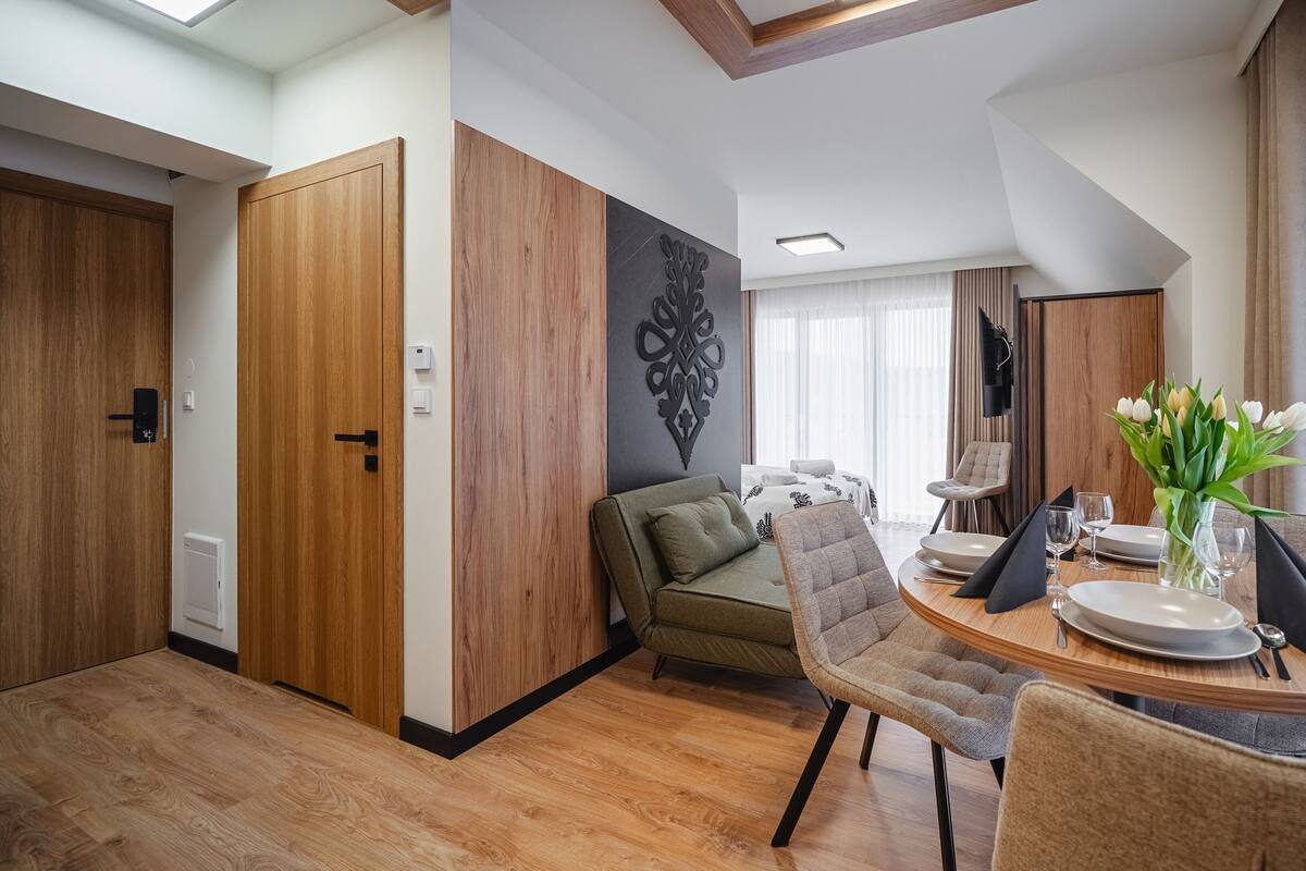A modern hotel room with a dining area, a sofa, a bed, and a decorative wall piece.