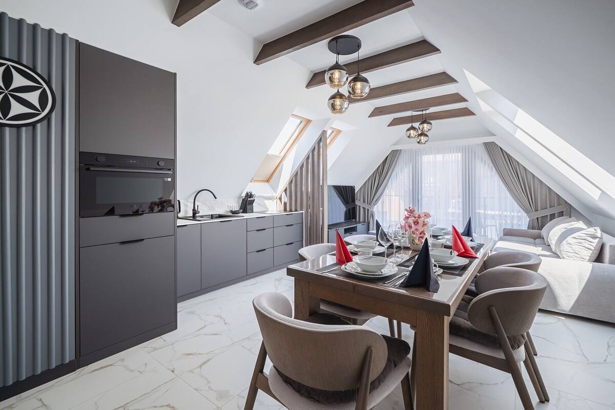 A modern kitchen with a built-in oven, a dining area with a table set for four, and a loft bedroom with a view.