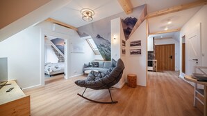 Ein geräumiges Loft mit hohen Decken, einer gemütlichen Sitzecke mit Schaukelstuhl, einem Esstisch und einer Treppe zu einer oberen Ebene.