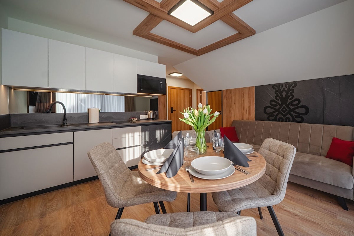 A modern kitchen with a dining area, wooden ceiling, and a decorative wall piece.