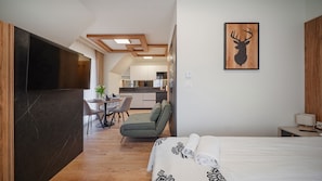 Ein modernes Hotelzimmer mit Bett, Fernseher, Essbereich und einer Küche im Hintergrund.