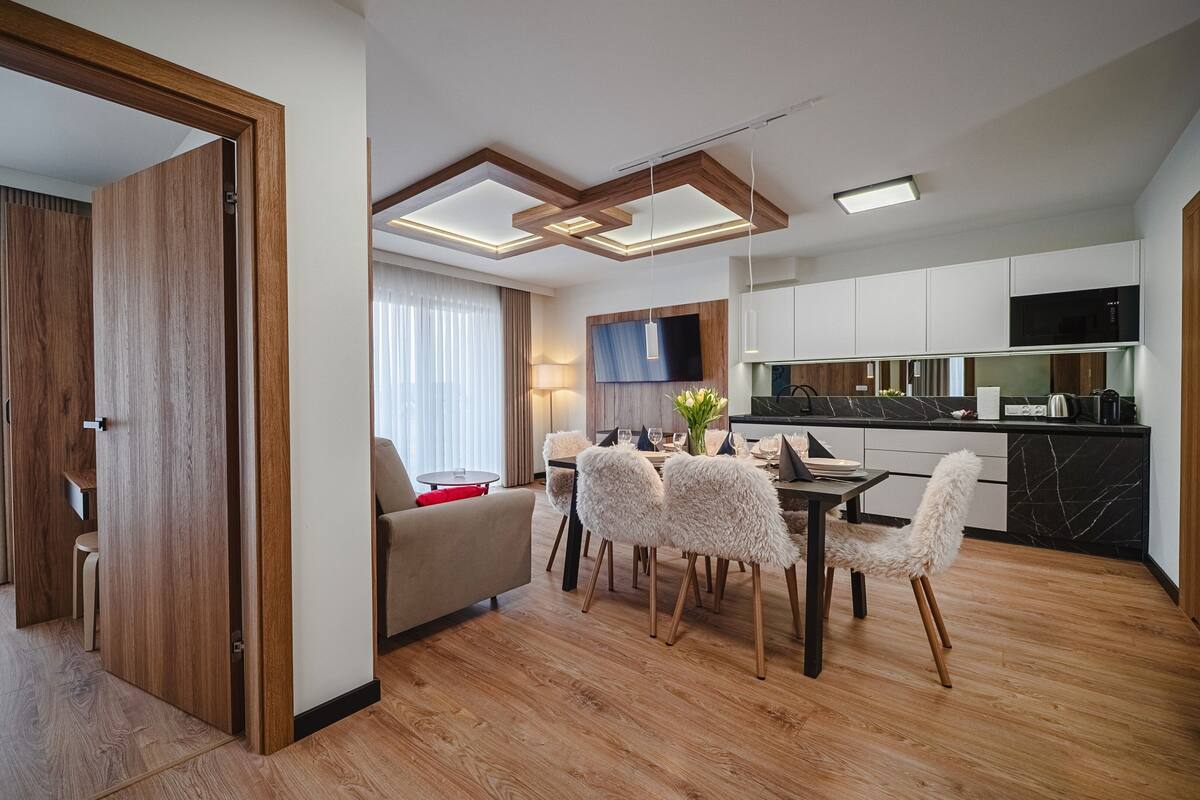 A modern hotel room with a dining area, wooden flooring, and a TV mounted on the wall.