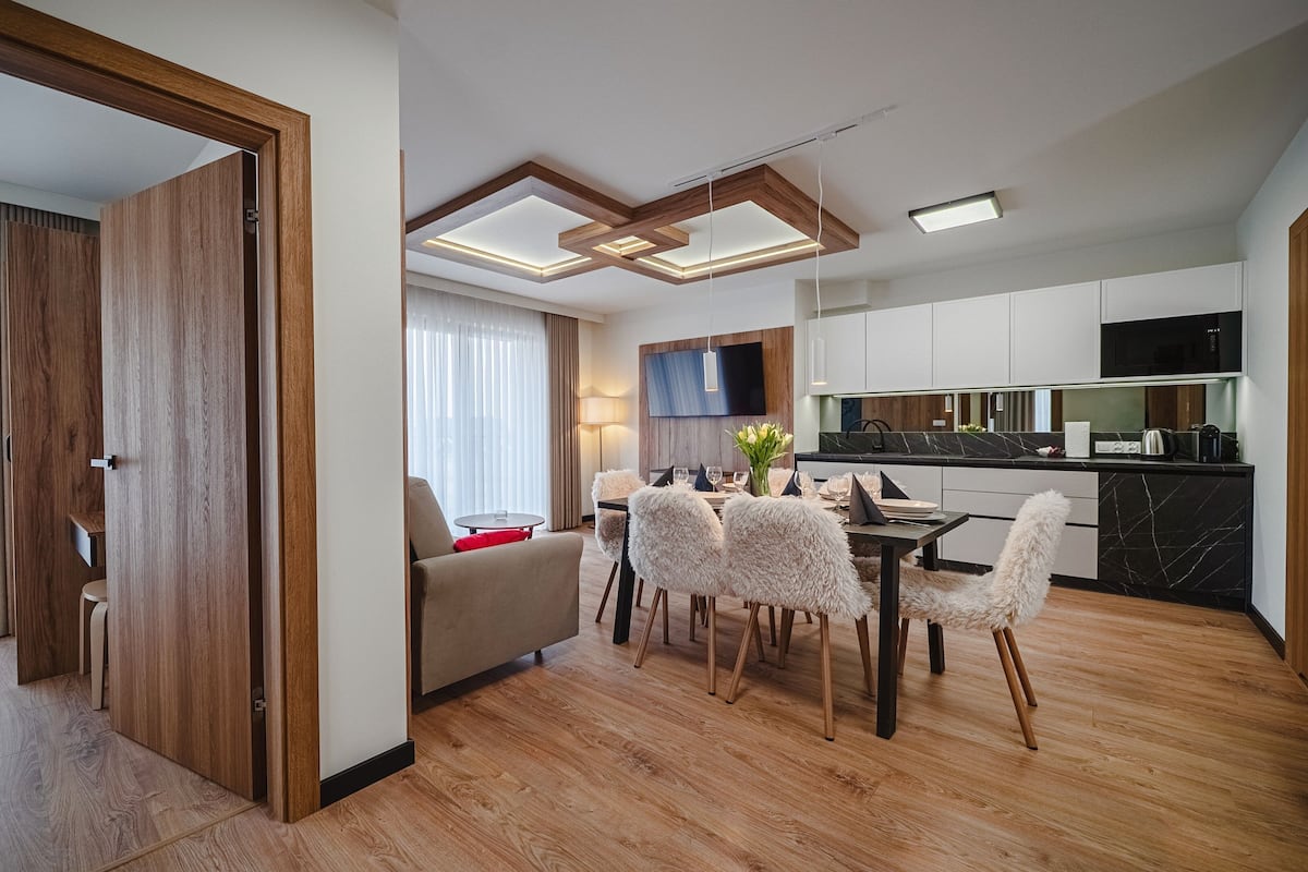A modern hotel room with a dining area, wooden flooring, and a TV mounted on the wall.
