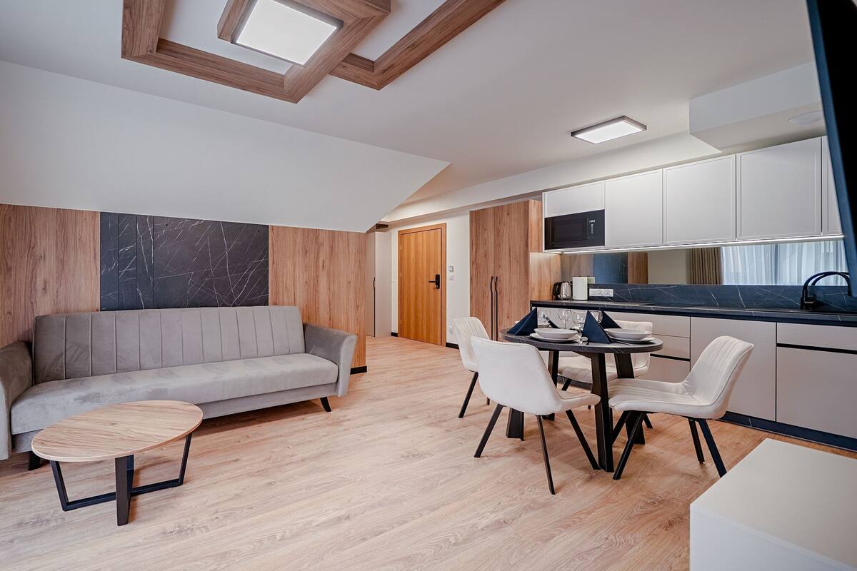 A modern living room with a sofa, a small round table, and a dining area with chairs.