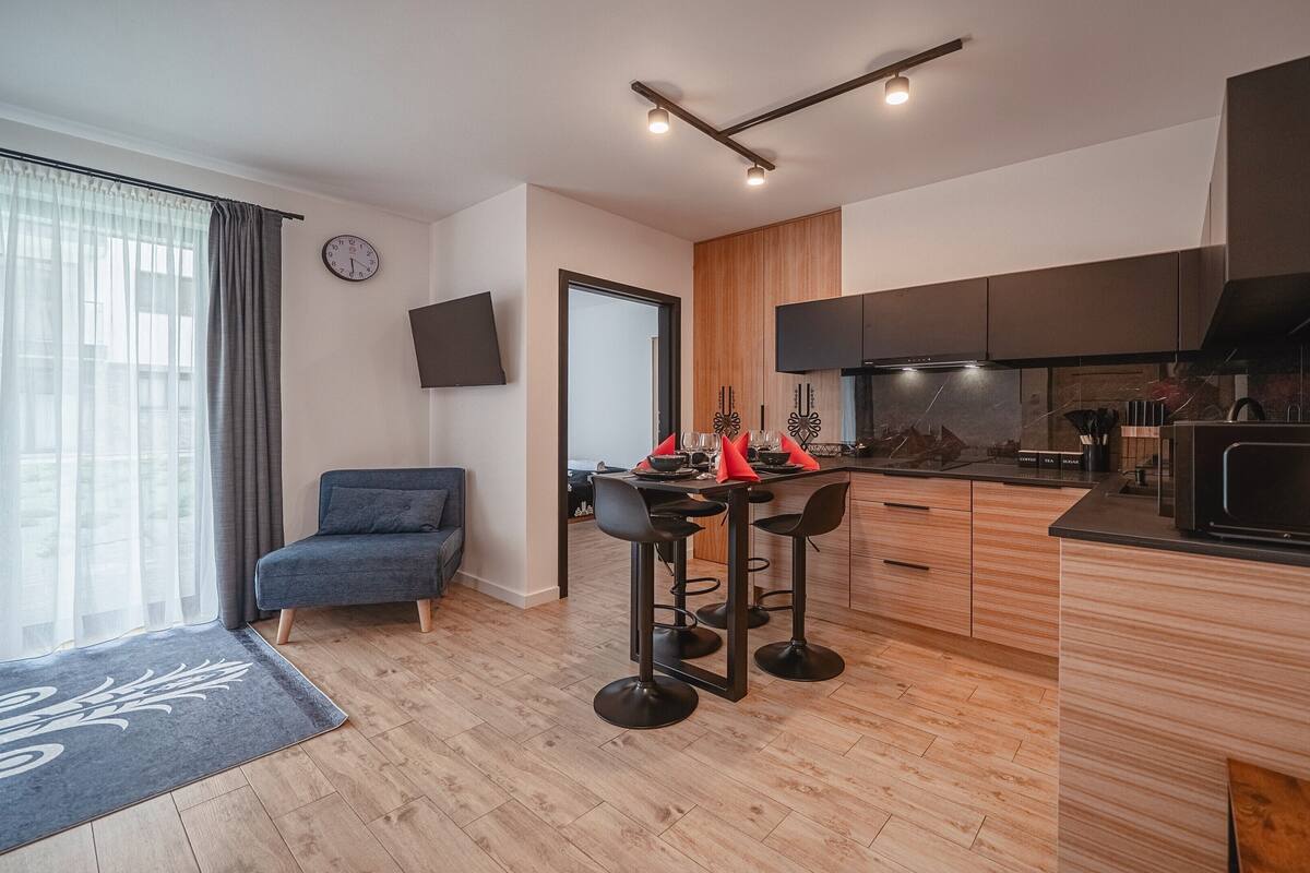A modern kitchen with a flat-screen TV, wooden cabinets, and a built-in microwave.