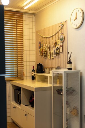 Une cuisine équipée d’un four à micro-ondes, d’une machine à café, d’une horloge et d’un calendrier accroché au mur.