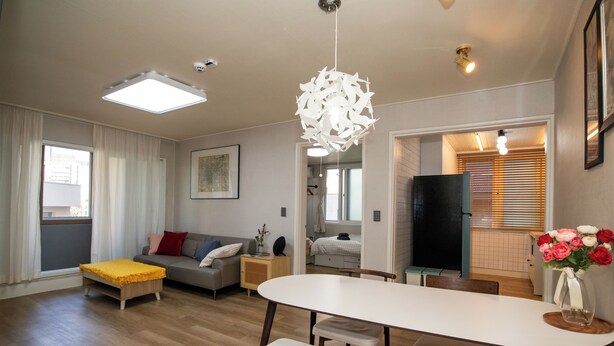 En moderne stue med sofa, spisebord og et køkken, der kan anes gennem en åben dør.