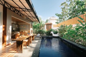 A pool with a swan float, wooden deck, and a dining area with chairs and a table. - Villa Casa de Sonya (Kutuh)