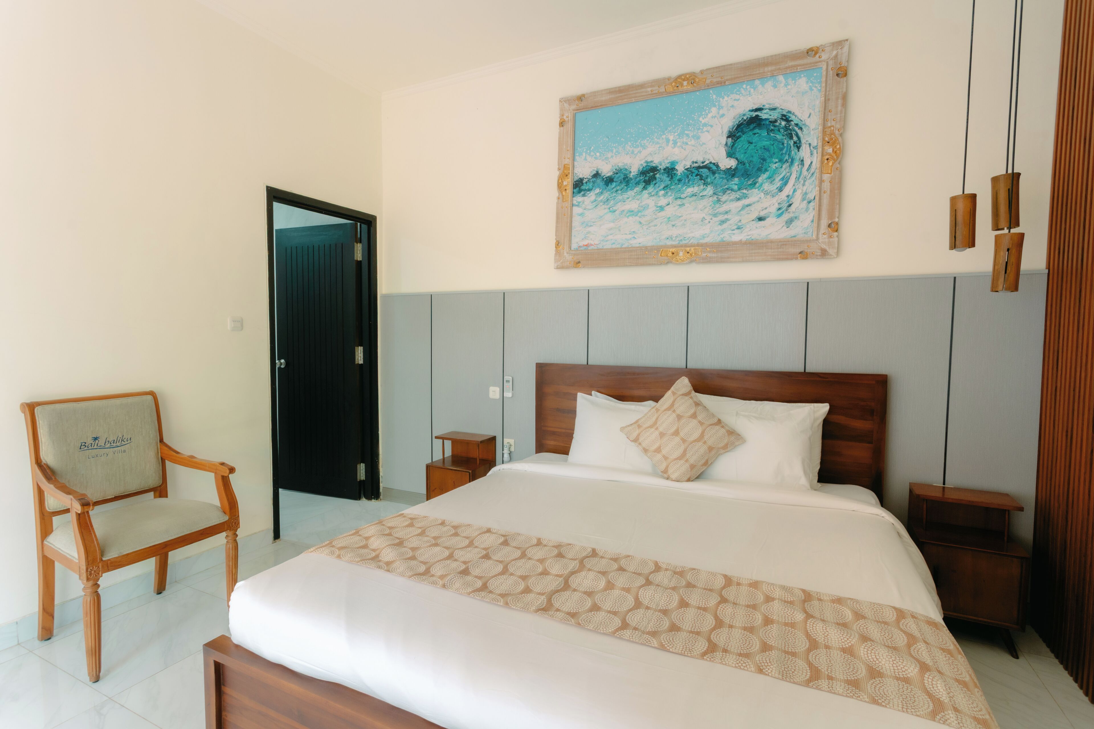 Un cuarto de hotel con una cama, una silla, una mesita de noche, un cabecero de madera y un cuadro en la pared.