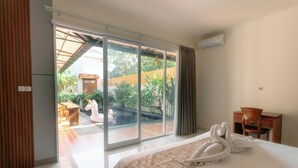 Habitación de hotel con cama, escritorio, silla, un amplio ventanal corredero que da a una zona de piscina y un equipo de aire acondicionado en la pared.