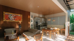 Una sala moderna con sofá, una mesa de centro, una mesa de comedor y sillas. Hay una zona de cocina con armarios y un refrigerador.
