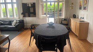 Una habitación con una mesa redonda, sillas negras, un armario de madera, un sofá negro y una ventana con cortinas.