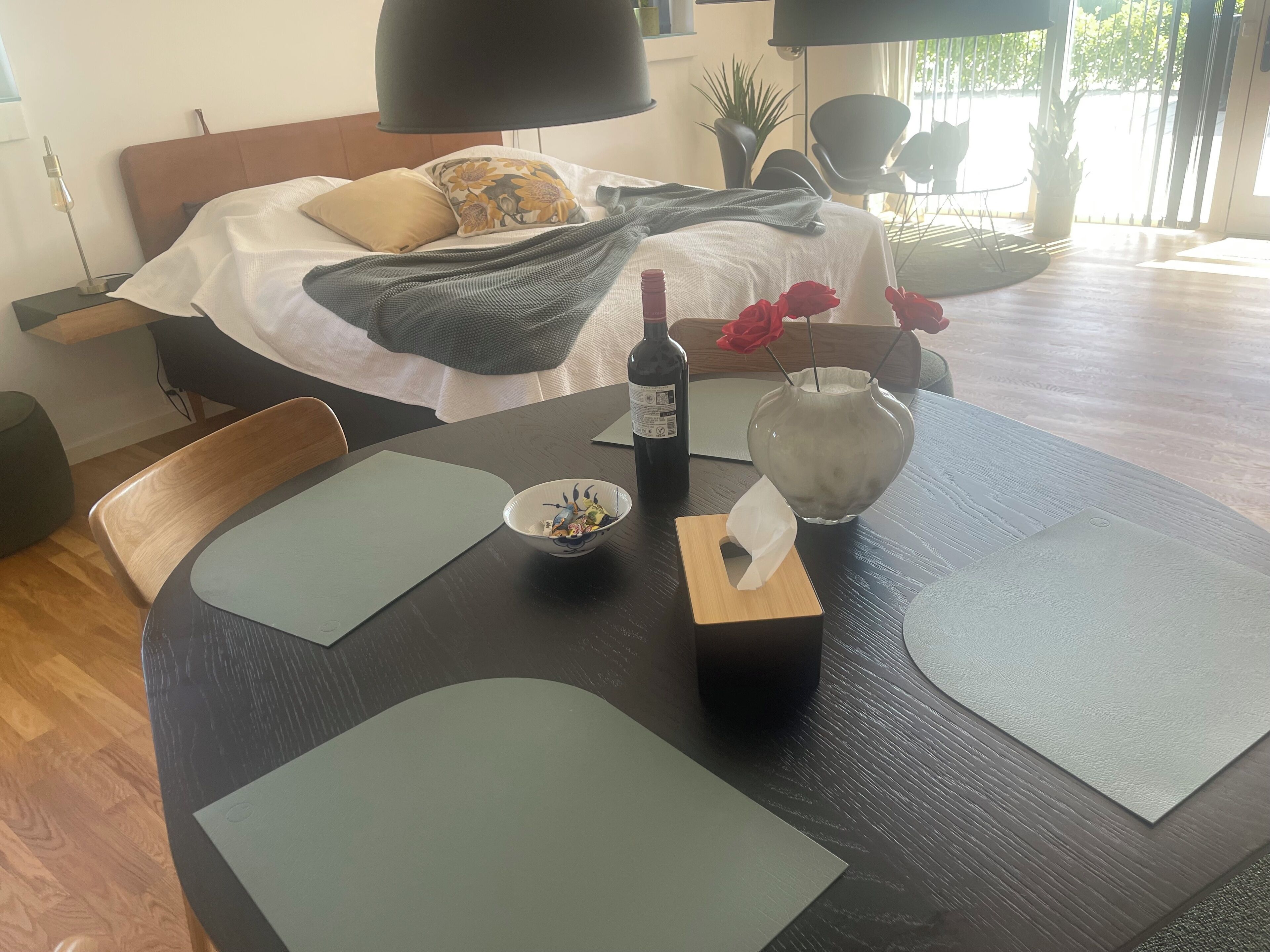 Un coin repas aménagé avec soin, avec une table dressée pour deux personnes, une bouteille de vin, un plat de nourriture et un vase rempli de roses rouges.