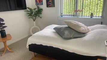 Quarto com cama, planta em vaso, obras de arte na parede e janela com vista para o verde.