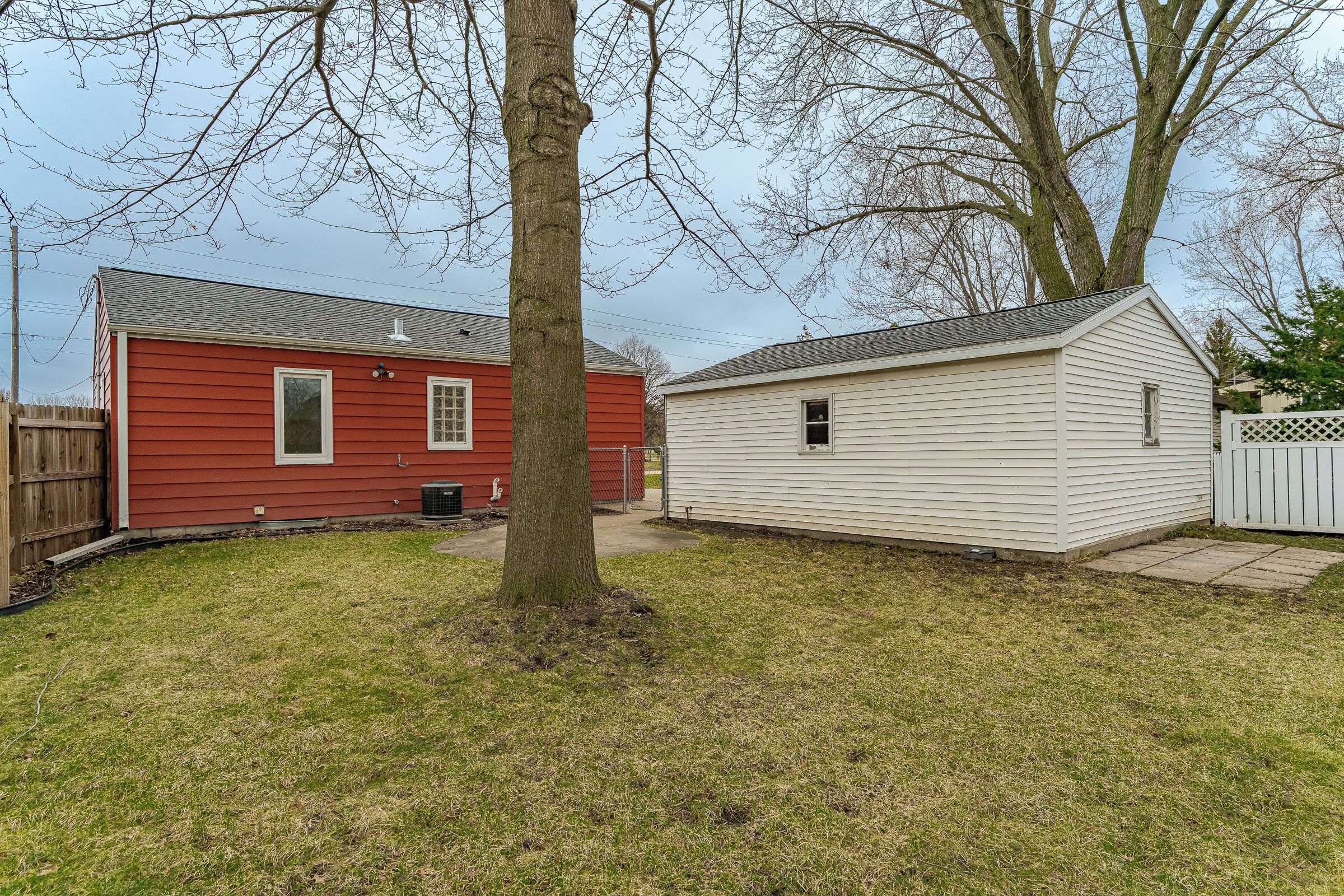 A red and white house with a small attached garage, a tree in the yard, and a wooden fence.