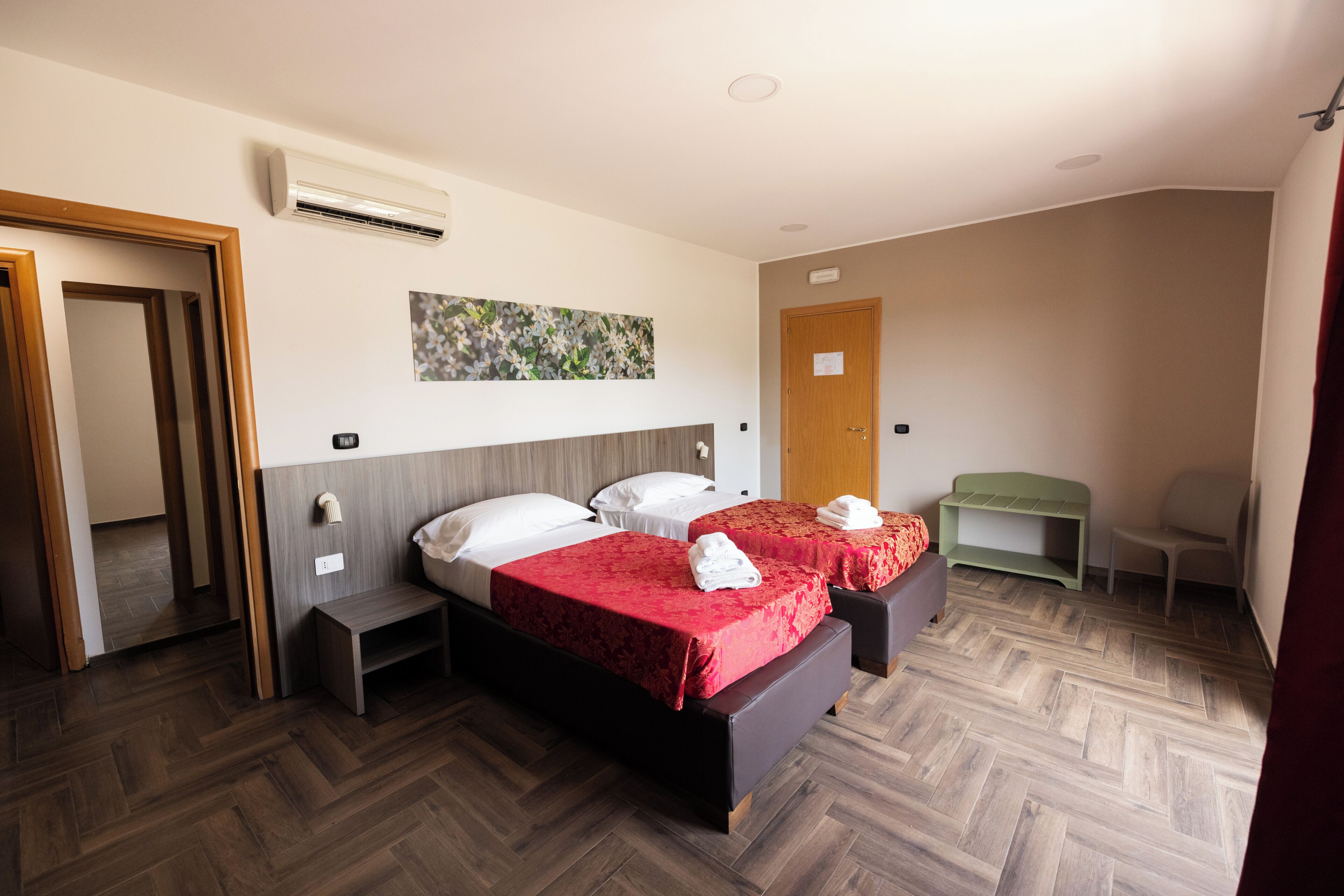 Una habitación de hotel con dos camas, piso de madera, un cuadro en la pared y una puerta.