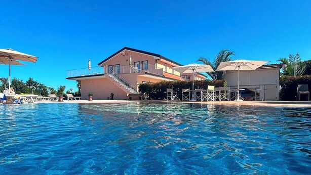Piscina azul cristalina com uma casa ao fundo.