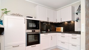A modern kitchen with white cabinetry, a built-in oven, a microwave, and a granite countertop. - Modern 93sqm on 2 levels for up to 4 people with its own sauna - (Sylt)