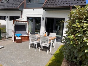 Eine Terrasse mit Tisch und Stühlen, ein überdachter Sitzbereich und ein Haus mit Ziegeldach und großen Fenstern.