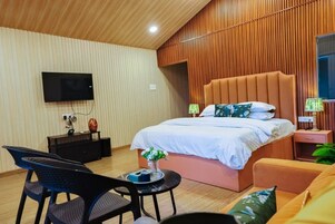 Quarto moderno com cama grande, televisão de tela plana, mesa pequena com um vaso e uma cadeira.