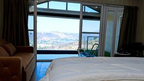 Camera da letto con un letto grande, un divano e vista su un paesaggio montuoso attraverso una porta scorrevole in vetro.