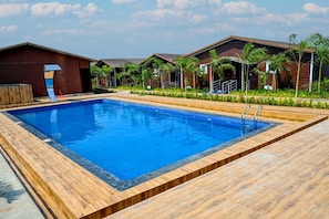 Une piscine avec une terrasse en bois, des bâtiments modernes et des palmiers.