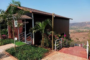 Um edifício com fachada vermelha, uma escadaria que leva a uma entrada coberta e vista da paisagem ao redor.