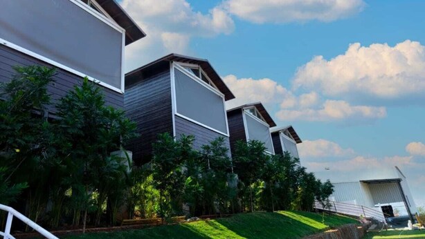Un edificio moderno con tetto spiovente, ampie finestre e un giardino curato con diverse piante.
