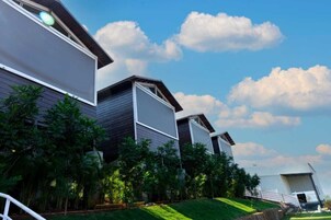 Um edifício moderno com telhado inclinado, grandes janelas e um jardim bem cuidado com diversas plantas.