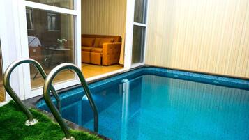 Une piscine avec une paroi en verre, un canapé à l’arrière-plan et une porte donnant sur une pièce.