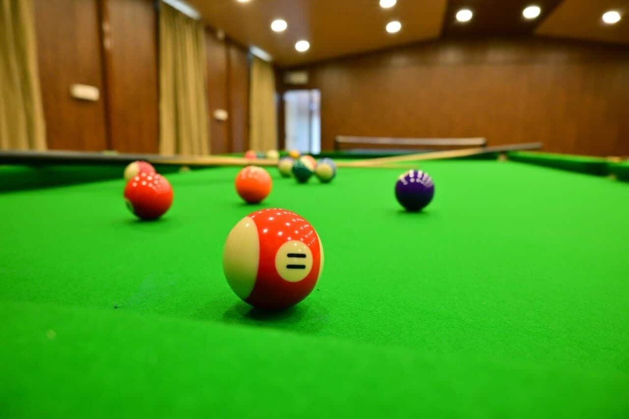 A pool table with balls in a room with wooden walls and ceiling lights.