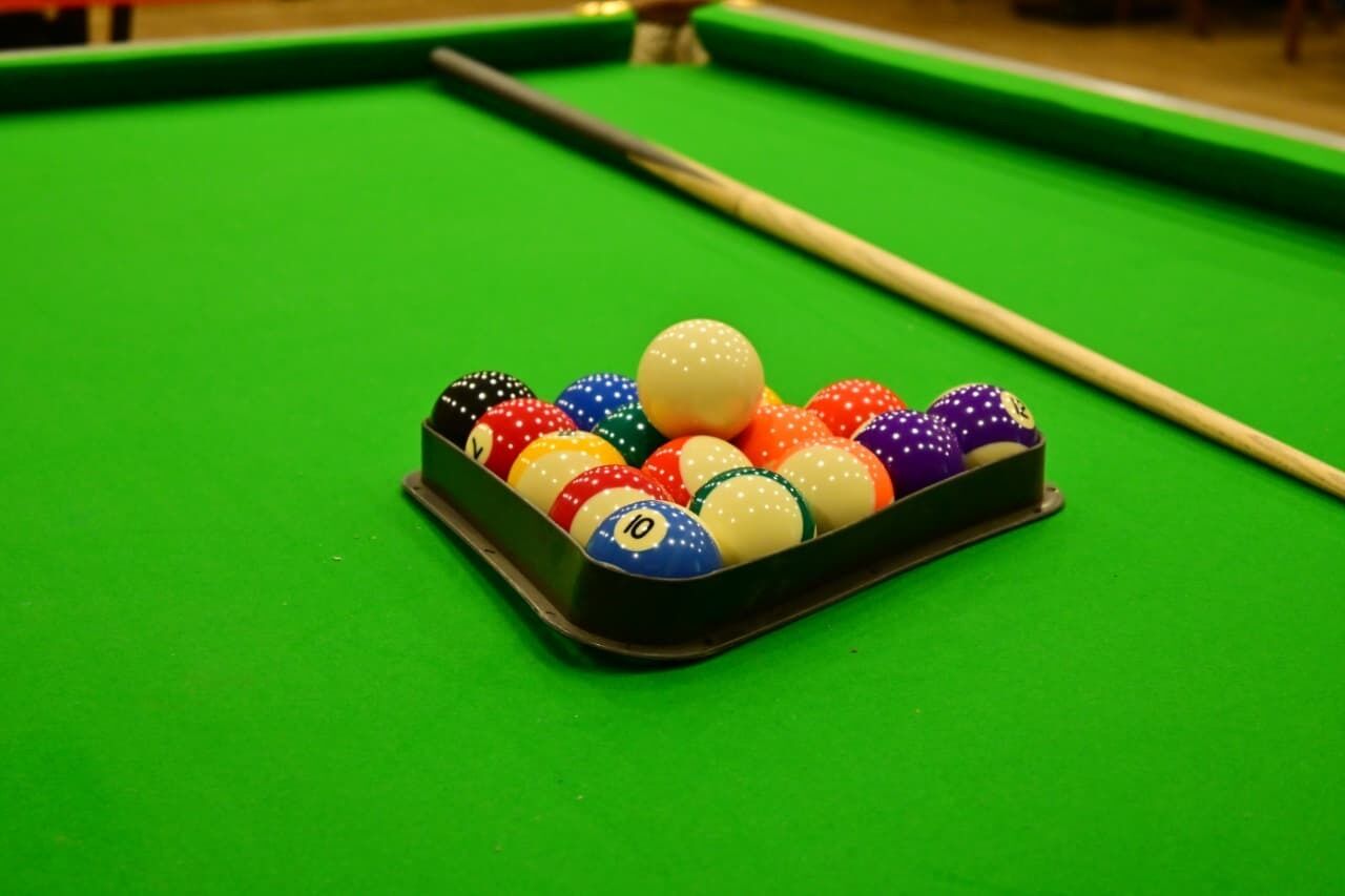 Una mesa de billar con un juego de bolas de colores y una vara.