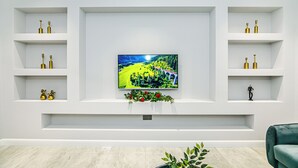 Una sala de estar moderna con un televisor de pantalla plana montado en una pared blanca, rodeada de estanterías blancas con objetos decorativos.