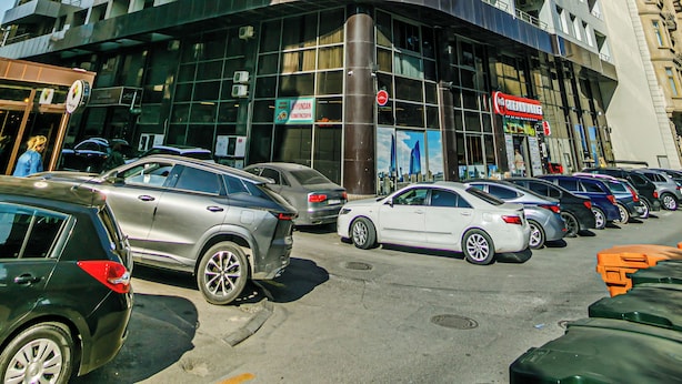 Un hotel de varios pisos con fachada curva, amplias ventanas y un estacionamiento con automóviles.