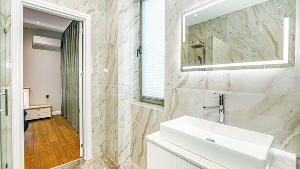A bathroom with a marble wall, a white sink, and a mirror. - Nizami Avenue Hotel (Baku)