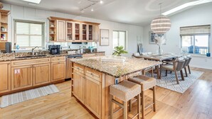 Une cuisine spacieuse avec des meubles en bois, un grand îlot central et un coin repas agrémenté d’un lustre.
