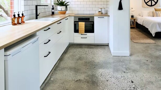 Een moderne keuken met witte kasten, een inbouwoven en een betonnen vloer.