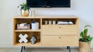 Een houten tv-meubel met een flatscreen televisie erboven. Het meubel heeft een lade en planken met verschillende items, waaronder boeken, een schedel en decoratieve objecten.