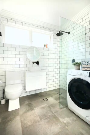 A modern bathroom with a toilet, sink, and washing machine. - Family‑friendly beach retreat in central Cronulla, just 350m from the beach U3 (Cronulla)